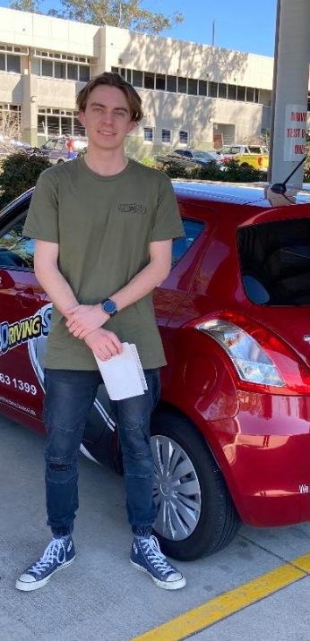 A new driver holding test paperwork beside a red Affordable Driving School car