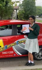 A new driver in school uniform holding a P plate beside a red Affordable Driving School car