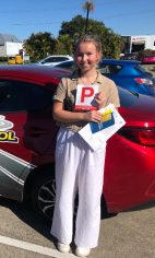 A new driver holding a red P plate and test sheet beside a red Affordable Driving School car