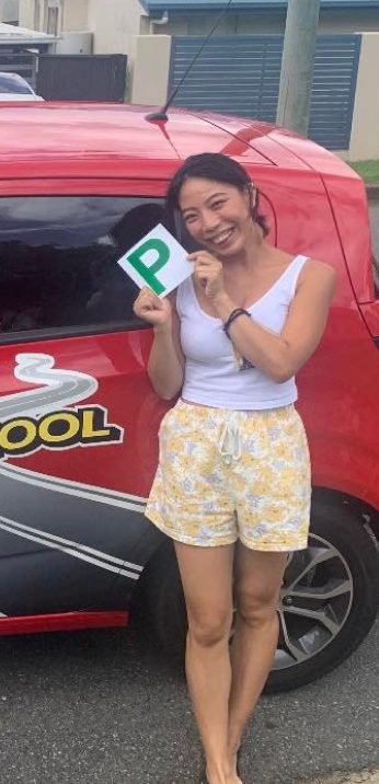A smiling new driver holding a green P plate beside a red Affordable Driving School car