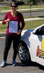 A new driver in sunglasses holding a test sheet beside a white Affordable Driving School car