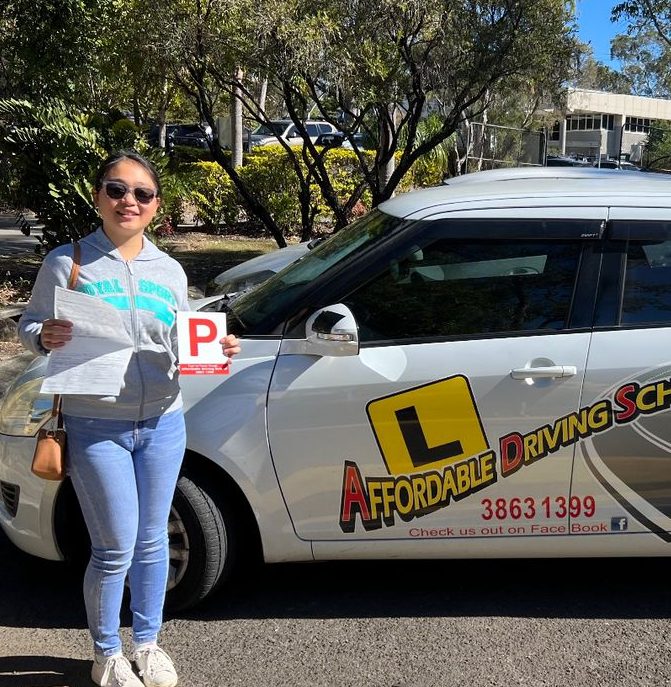 A new driver in sunglasses holding a P plate and test paperwork beside a white Affordable Driving School car