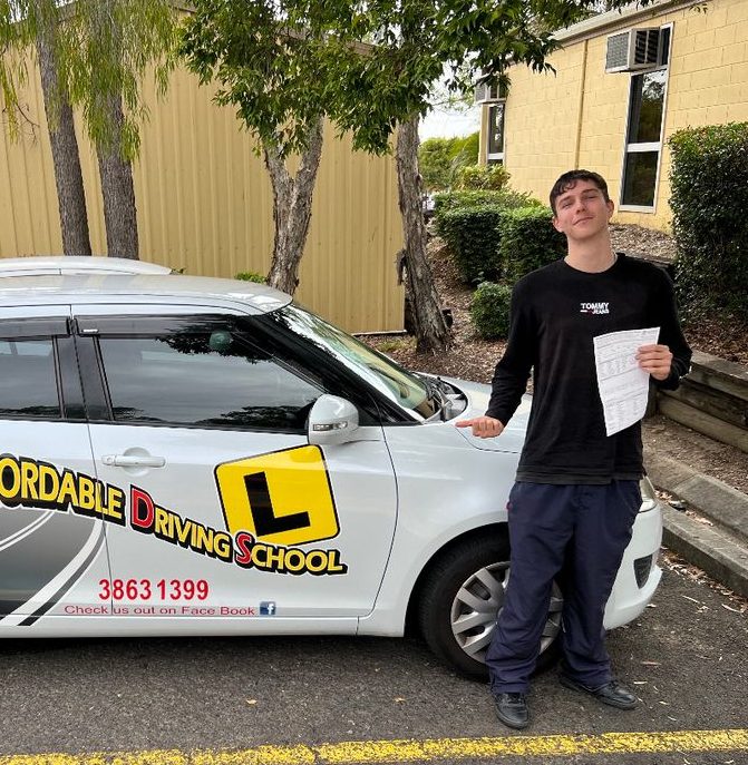 A new driver holding a test sheet beside a white Affordable Driving School car
