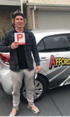 A new driver holding a red P plate beside a white Affordable Driving School car