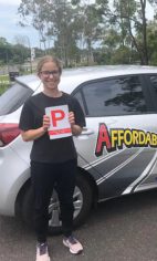 A new driver holding a red P plate beside a white Affordable Driving School car