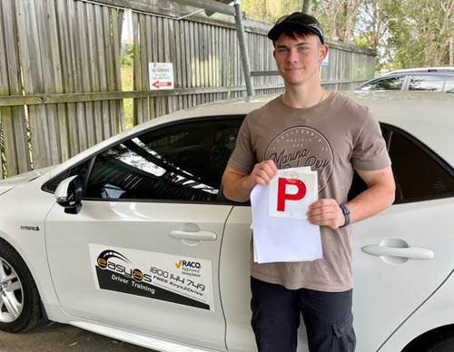 Young man in a cap holding a red P plate beside an EASYAS car