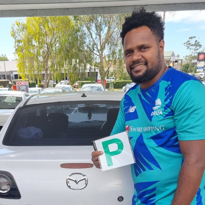 Man holding a green P plate beside a white Mazda