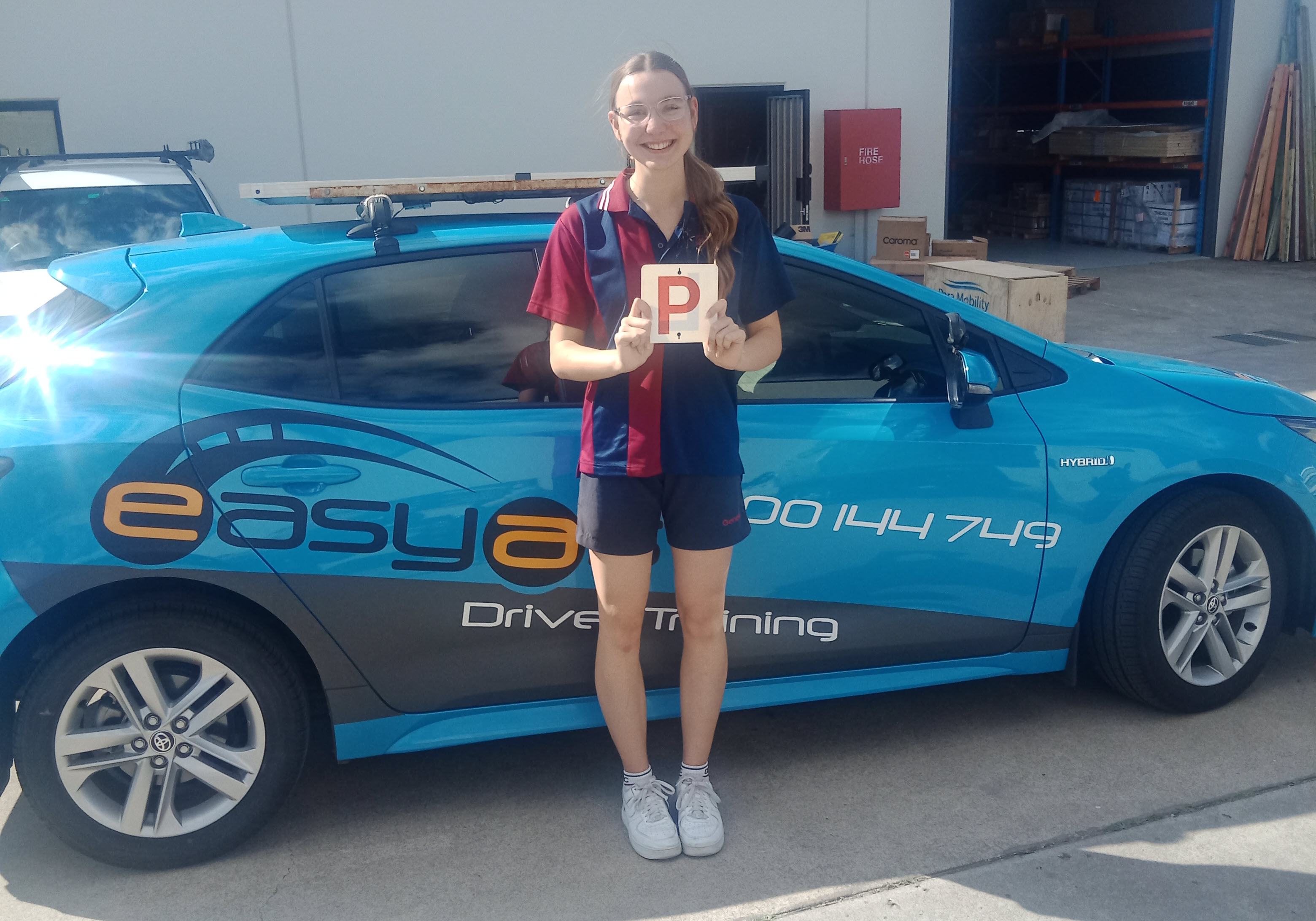 Young woman holding a red P plate beside a blue EASYAS car