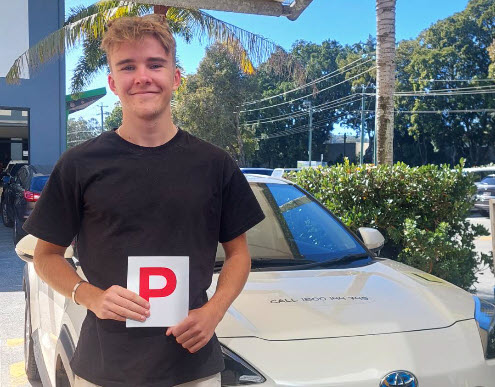 Young man holding a red P plate in front of a white Toyota
