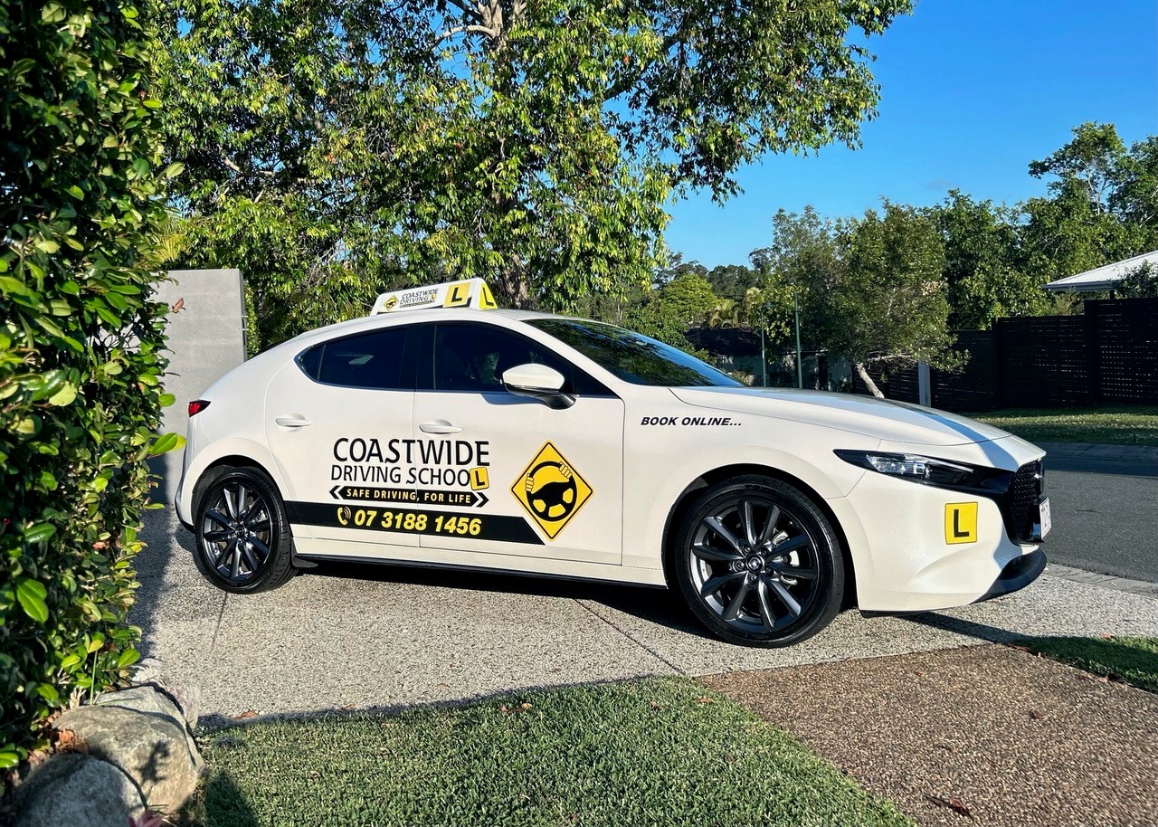 White Coastwide Mazda learner car parked beside trees