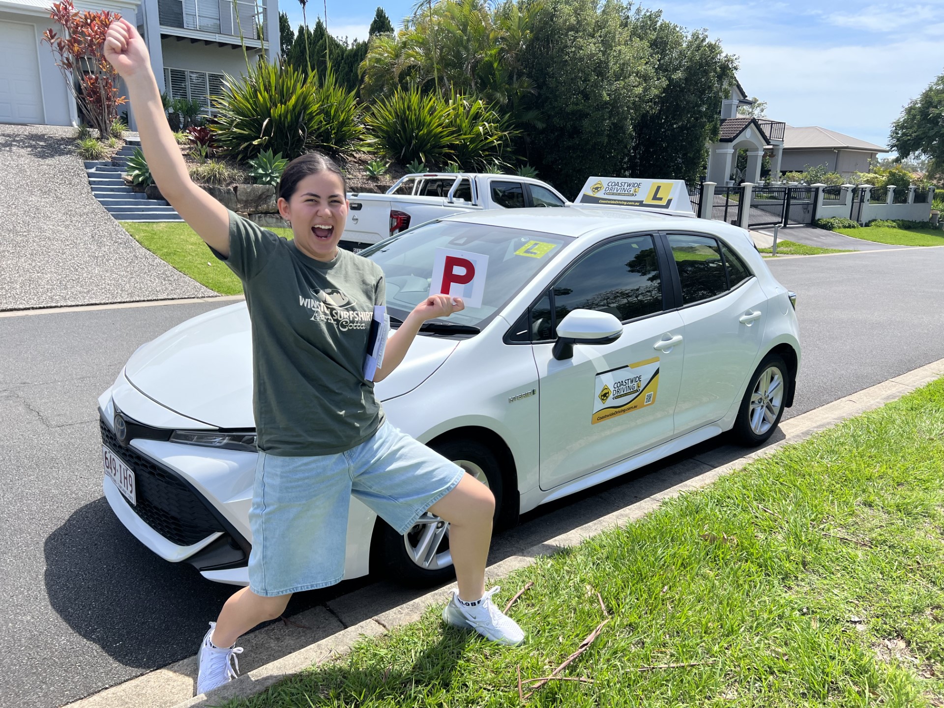 Person holding a red P plate beside a white Coastwide hatchback
