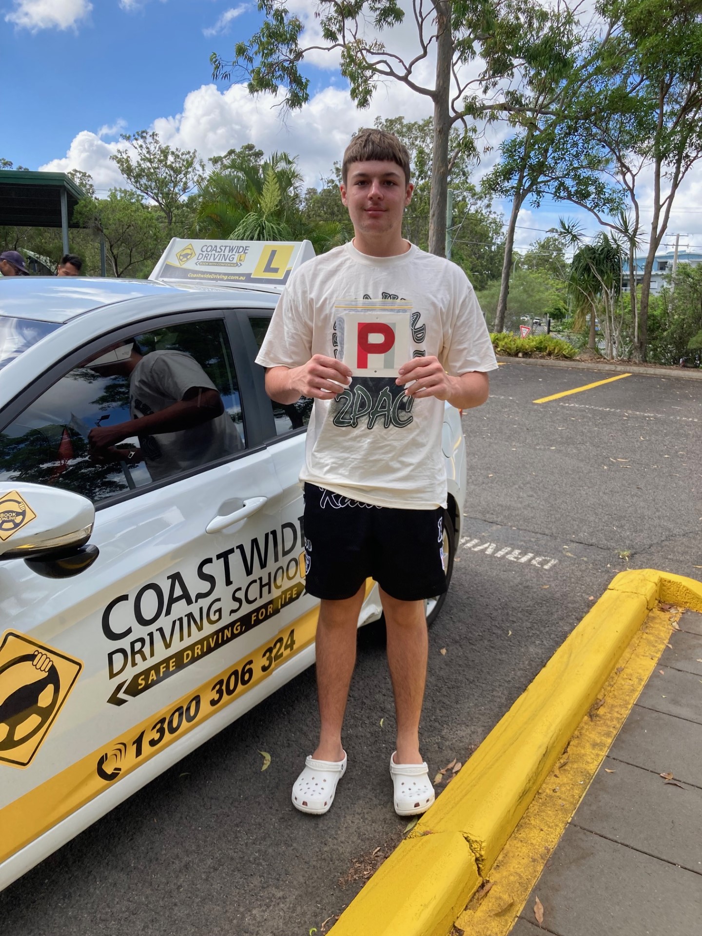 Person holding a red P plate beside a Coastwide learner car