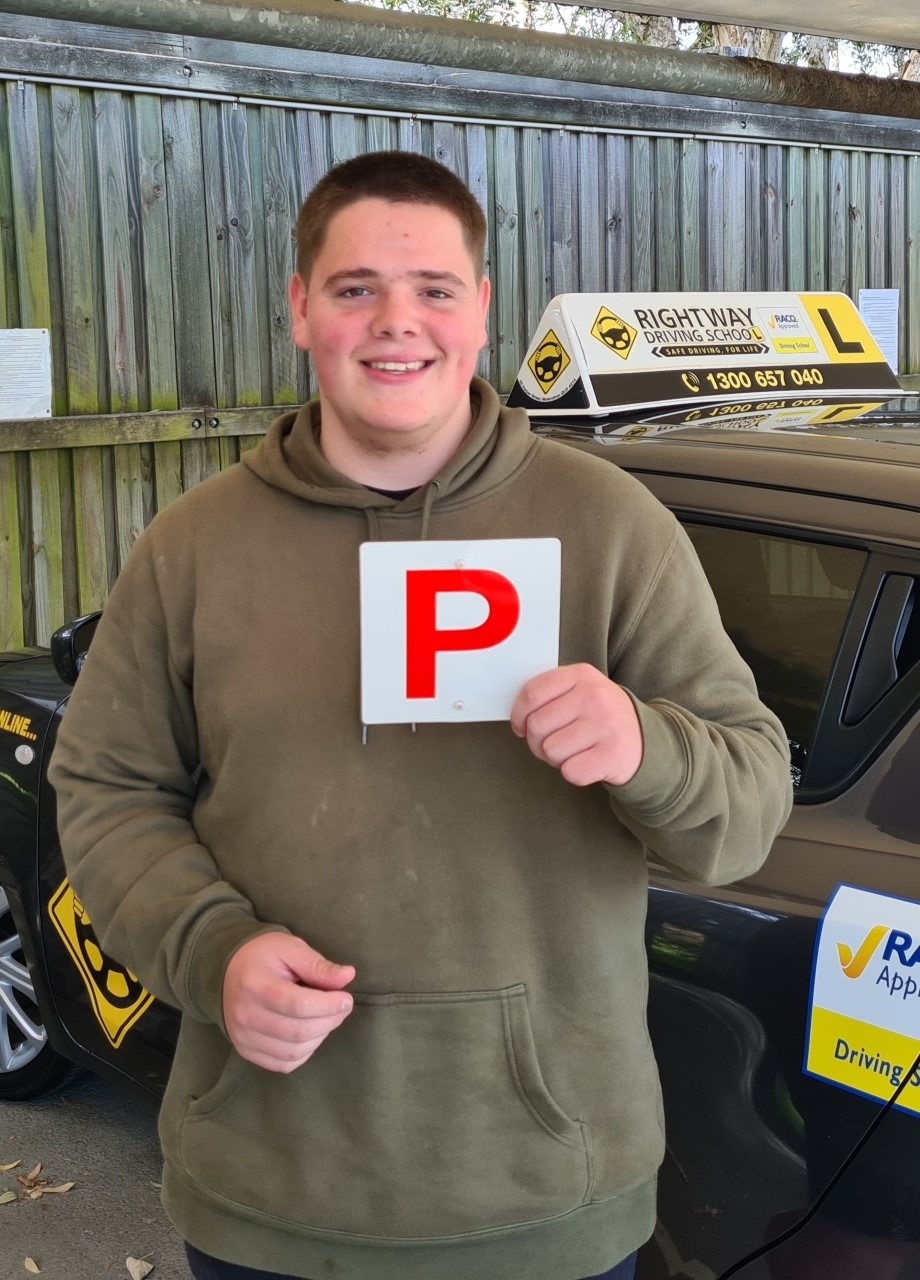 Person in a green hoodie holding a red P plate beside a dark car with a Rightway roof sign.