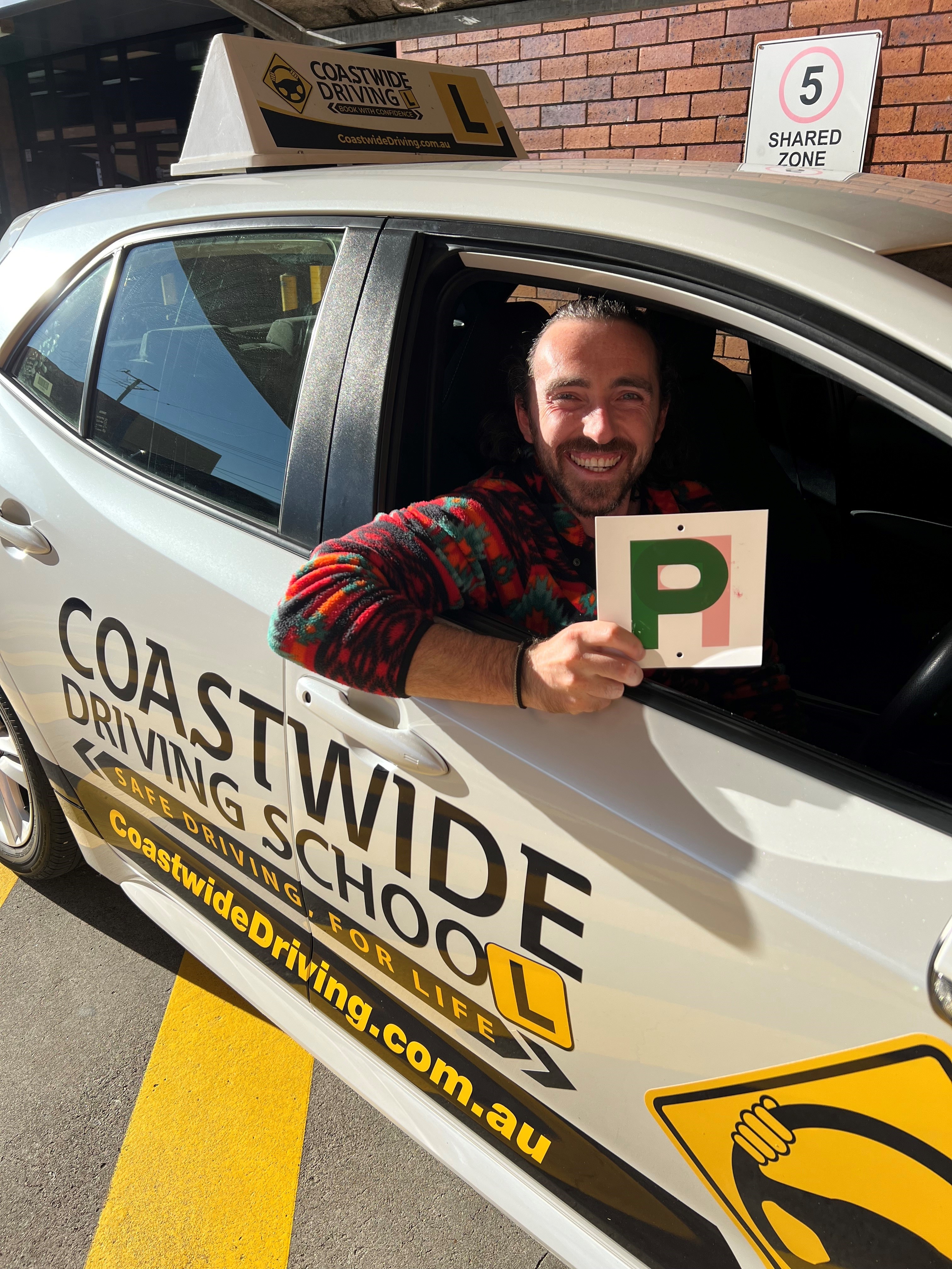 Person holding a green P plate at the window of a Coastwide car