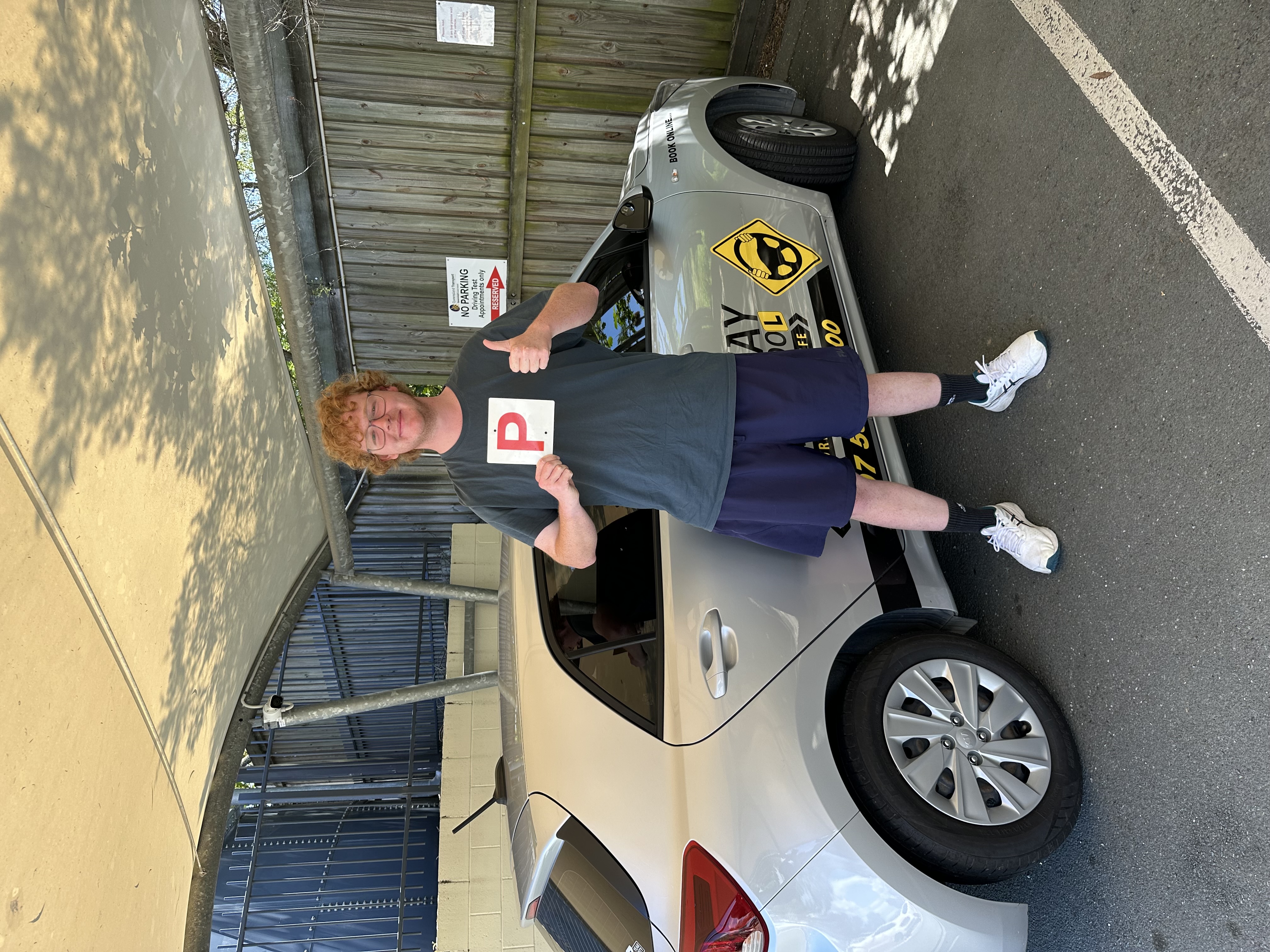 Person in a dark top holding a red P plate beside a silver Rightway car