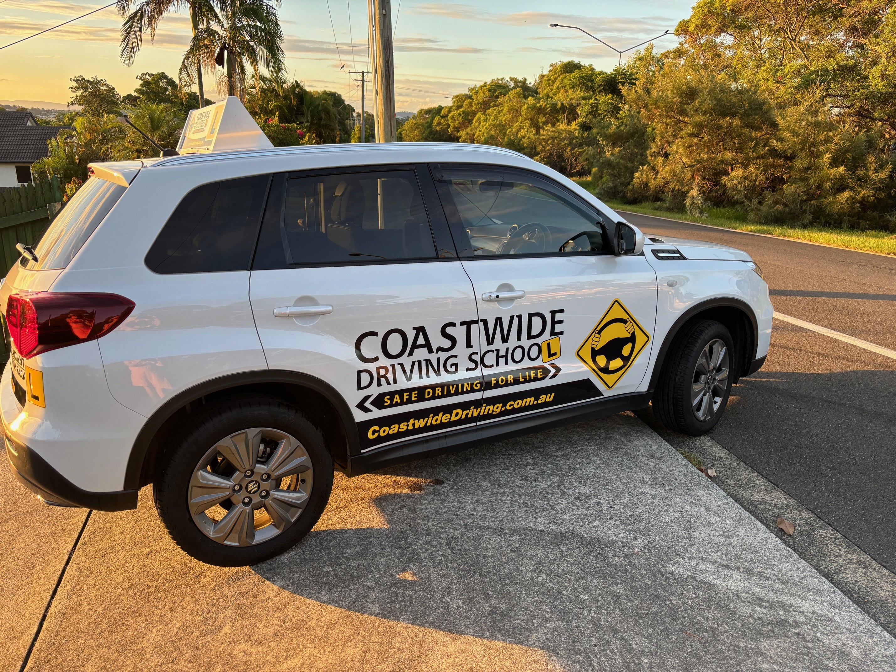 White Coastwide Suzuki learner car parked beside a kerb