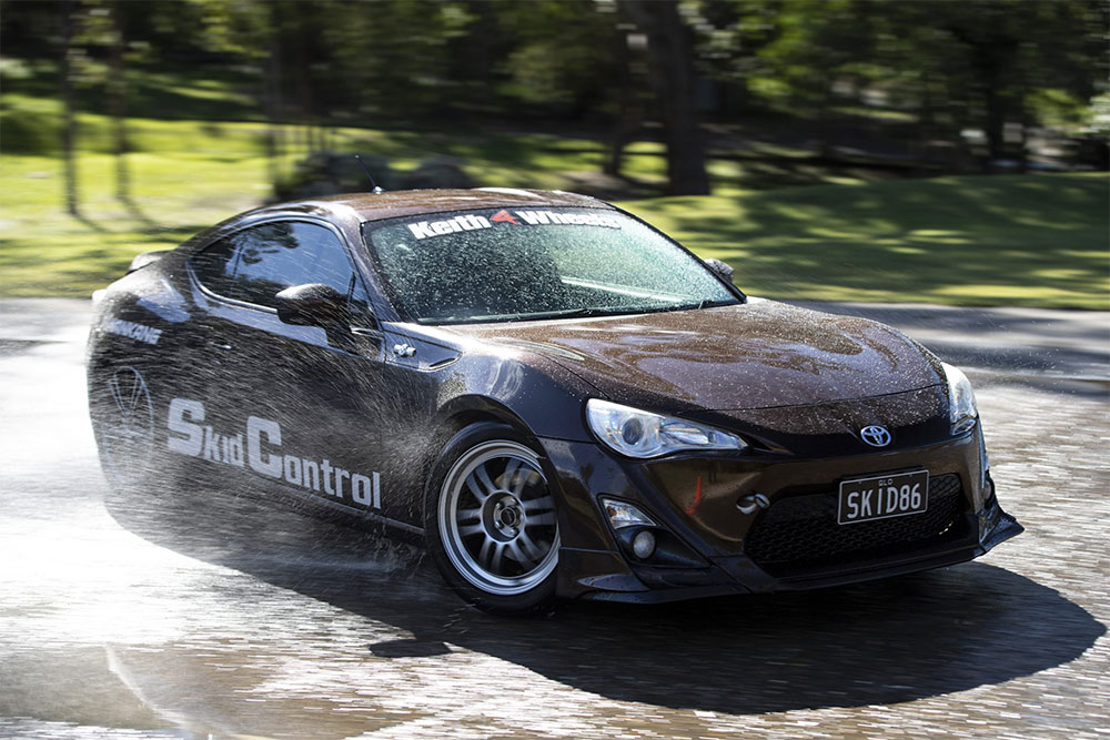Black Skid Control car spraying water on a skid pan.