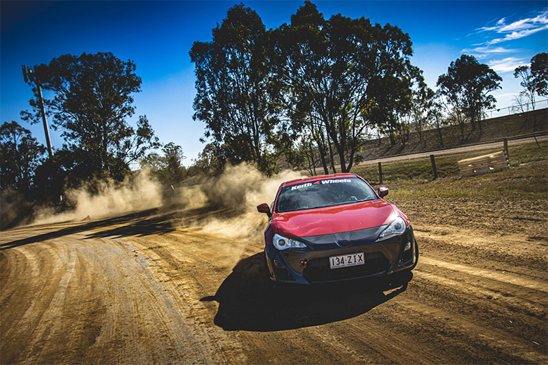 A car drifts over a dirt track, creating a cloud of dust behind it.