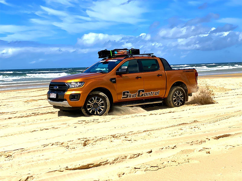Orange Ford Ranger Wildtrack driving on a sandy beach.