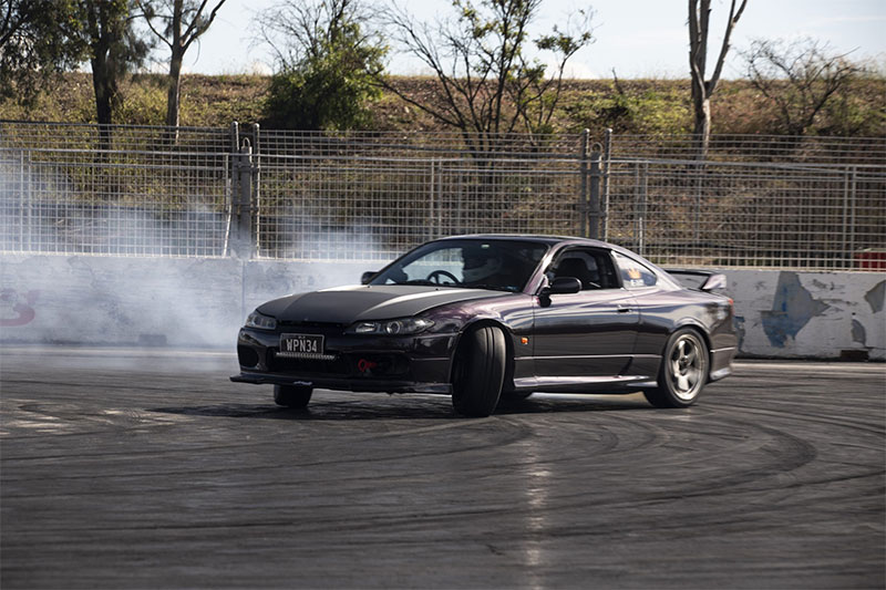 Black car drifting on a track with tyre smoke behind it.