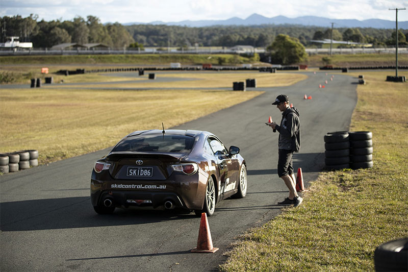 Driver of a black car receives instructions from a professional instructor on a race track.