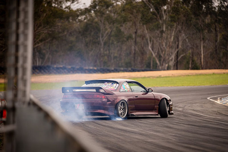 Burgundy car drifting around a corner of a track.