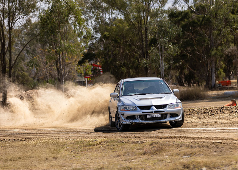 White car sliding around a gravel and dirt corner on a rally track.