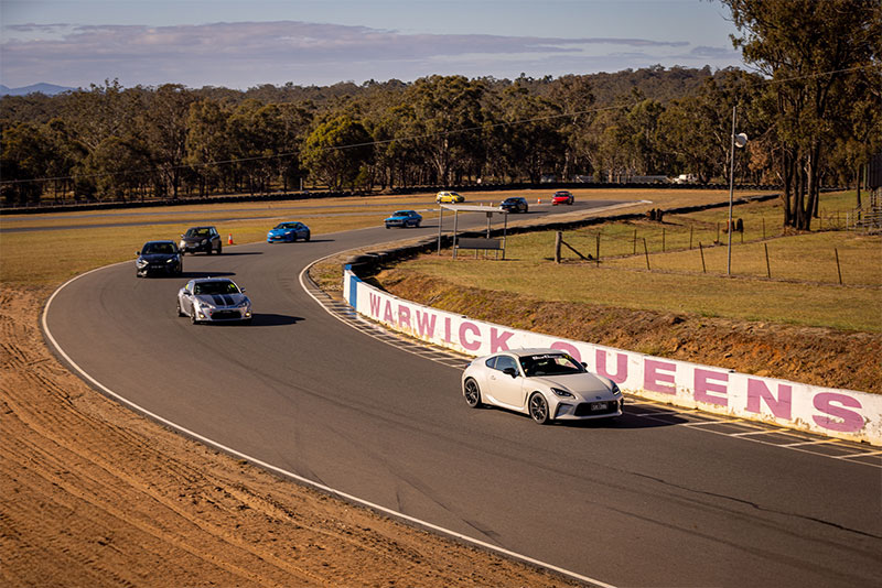 Overhead view of a race track with multiple cars driving around a corner.