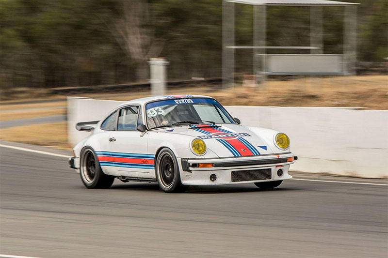 A vintage white car with a stripe, going around a race track.