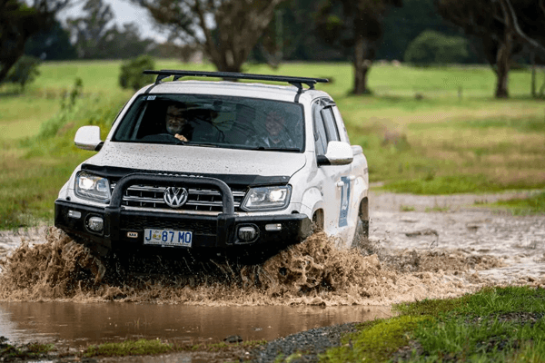 A white 4x4 car splashes through a muddy puddle.