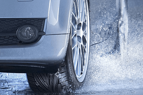 A white car splashes through a puddle.