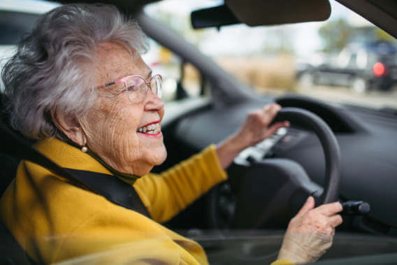 A happy older woman hold a steering wheel and checks her mirror in a car.