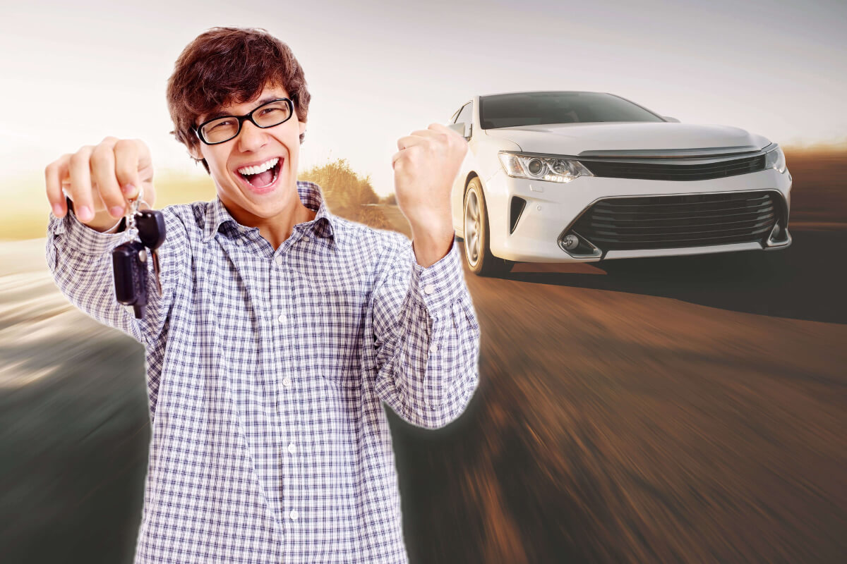 An excited man celebrates with a key in his hand as a white car drives past.