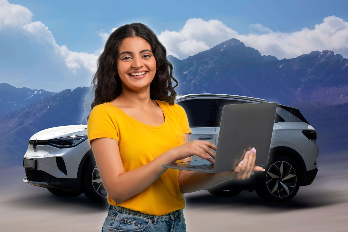 A happy woman stands holding her laptop, with her car and mountains behind her.