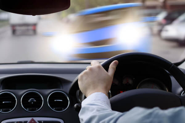 Hand holding steering wheel as a blurry car approaches head on.