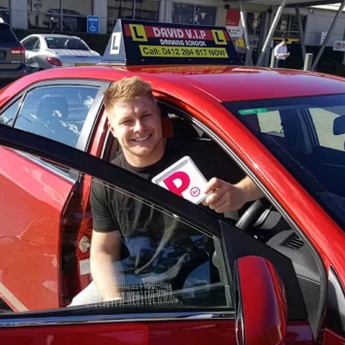 Happy student sits in a red Driving Lesson car after passing his Driving Test in Parramatta.