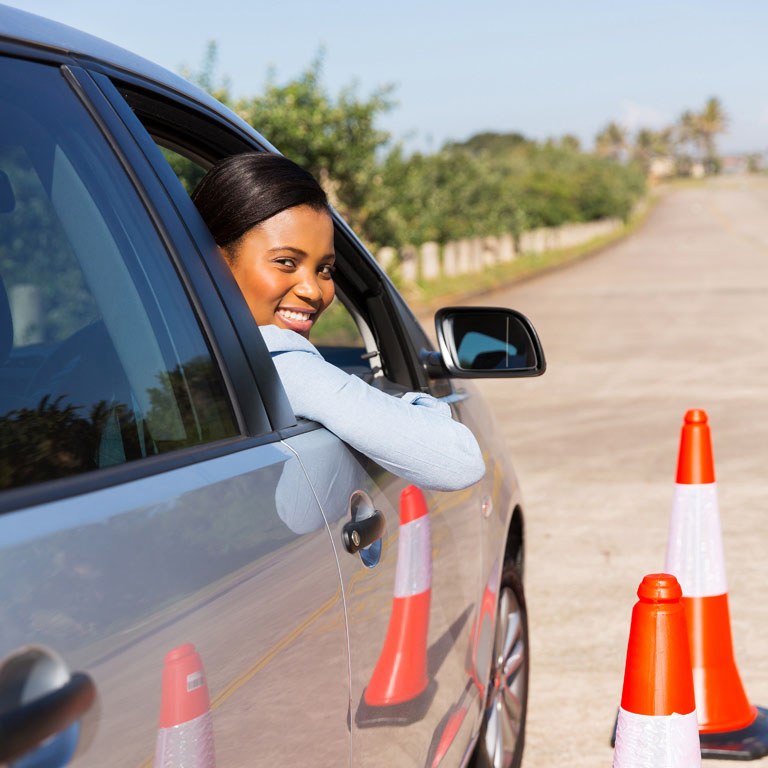Happy woman parked in a car, surrounded by traffic cones.