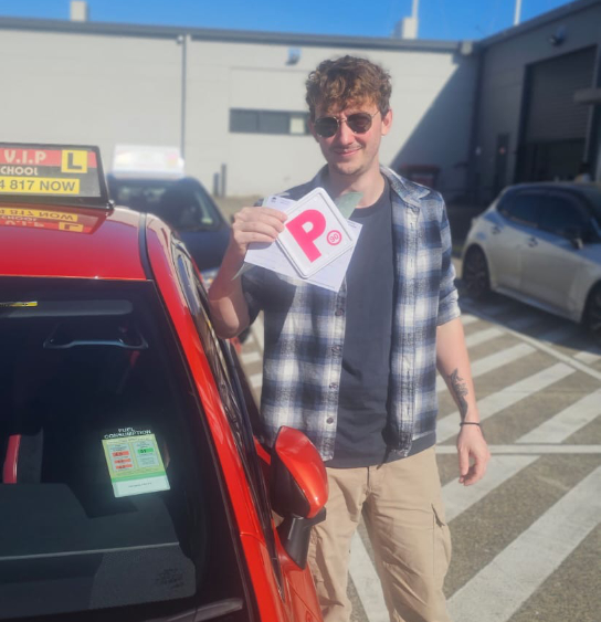Happy student in sun glasses stands in front of a red Driving Lesson car after passing his Driving Test in Parramatta.