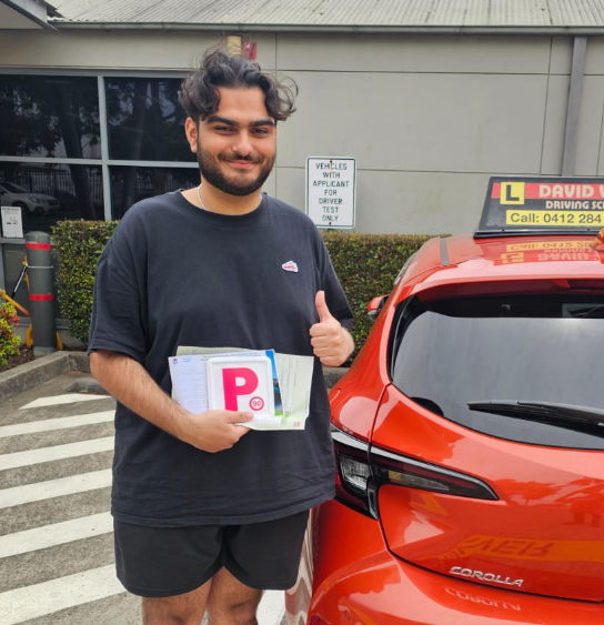 Happy student stands in front of a red Driving Lesson car after passing his Driving Test in Parramatta.