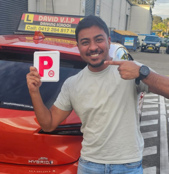 Happy student stands in front of a red Driving Lesson car after passing his Driving Test in Parramatta.