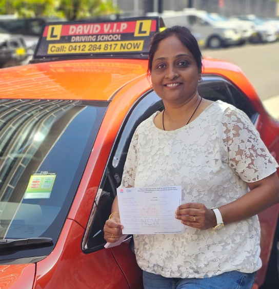 Smiling student stands in front of a red Driving Lesson car after passing her Driving Test in Parramatta.