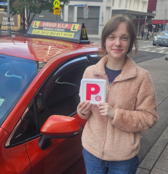 Happy student stands in front of a red Driving Lesson car after passing her Driving Test in Parramatta.
