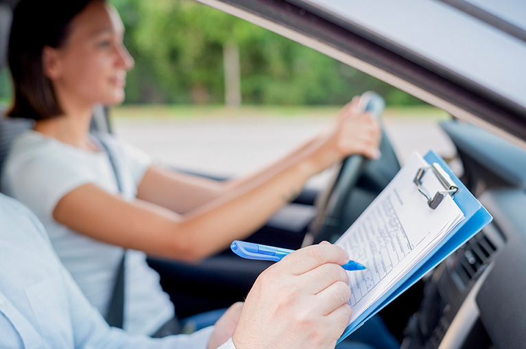 Driving instructor reviewing a checklist while a student practices behind the wheel.
