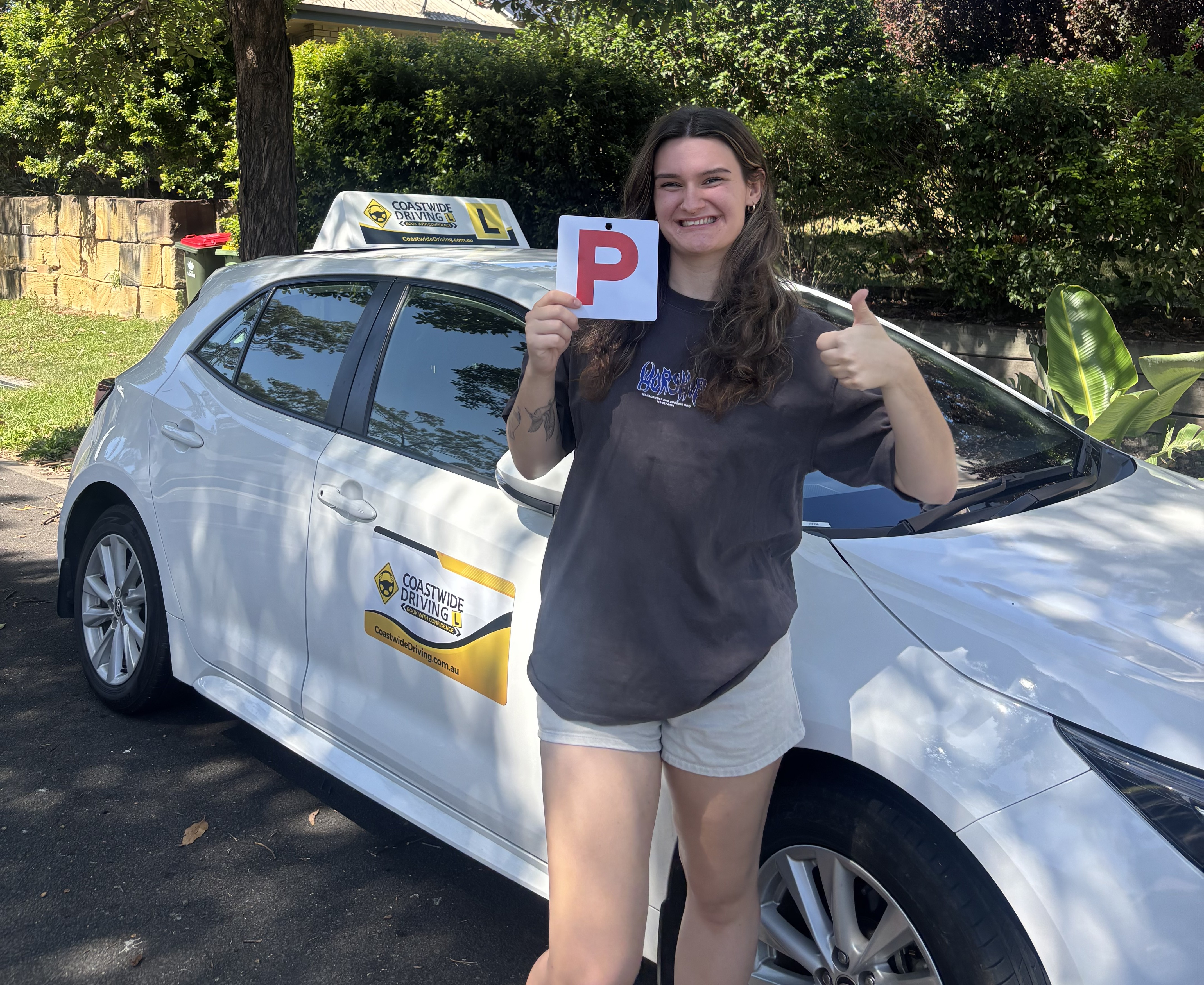 Person holding a red P plate in front of a white Coastwide car