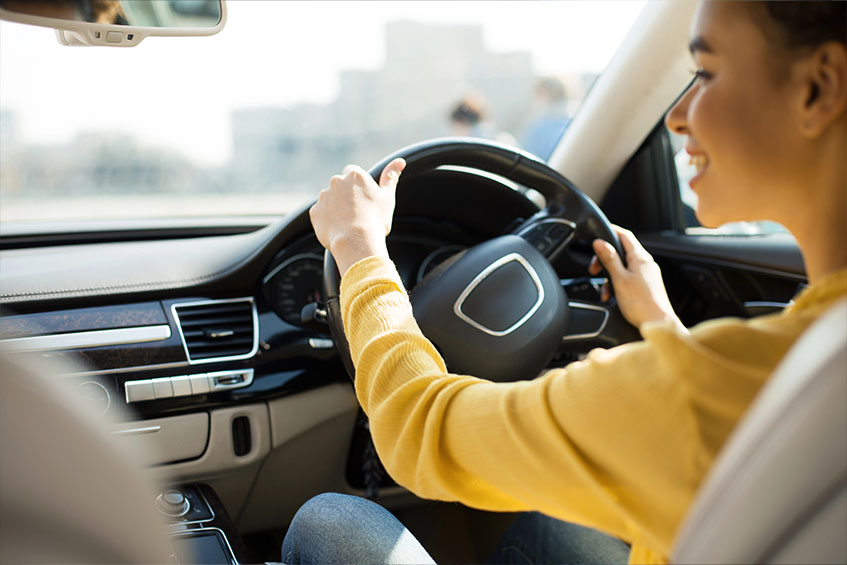 Happy student on a driving lesson with hands on steering wheel.
