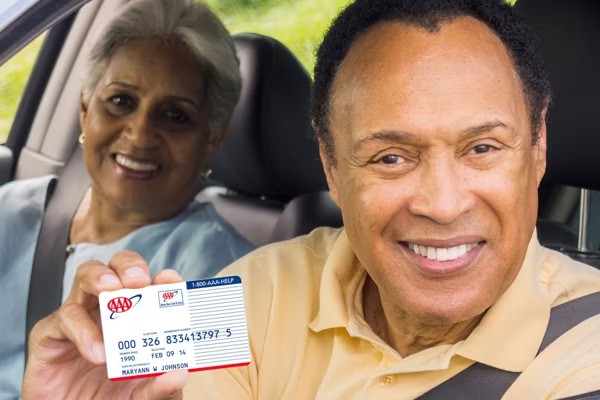 Two adult AAA members smiling in a car, one holding an AAA membership card