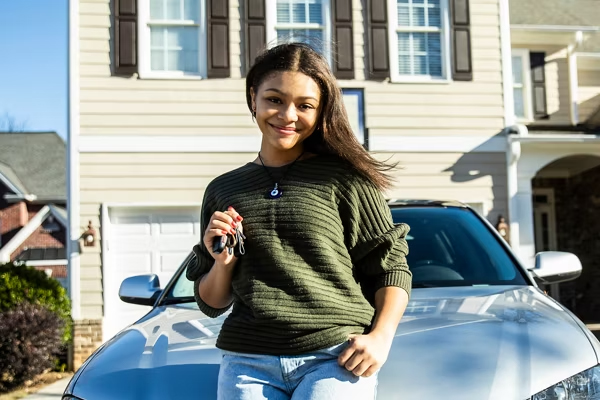 Teen driver standing beside a car, smiling and holding car keys.