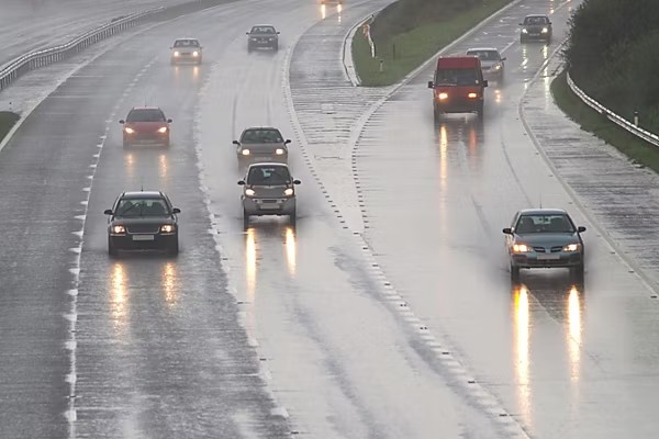 Cars driving on a wide wet road in rainy conditions.