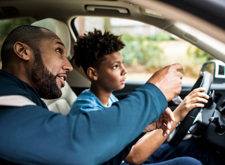 Adult instructor pointing ahead while a teen student practices driving.