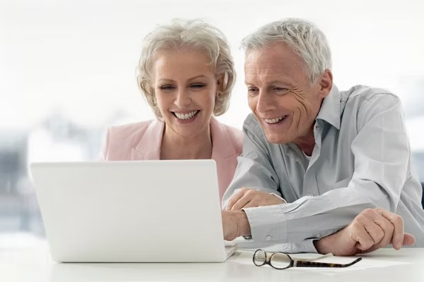 Two older adults smiling while viewing information on a laptop.